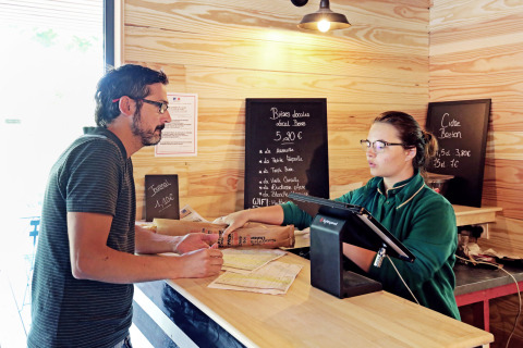 Uomo parla con receptionist al banco check-in di Huttopia Baie du Mont St Michel, villaggio vacanze in Bretagna.