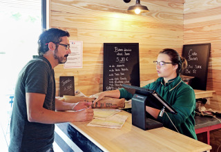 Uomo parla con receptionist al banco check-in di Huttopia Baie du Mont St Michel, villaggio vacanze in Bretagna.
