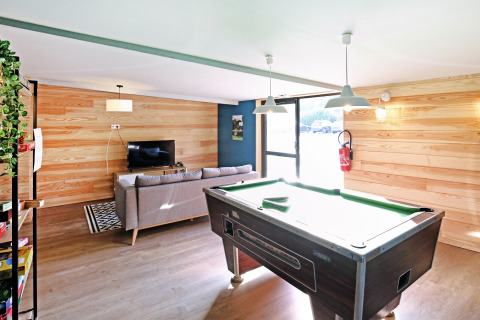Sala comune con tavolo da biliardo, divano e TV presso Huttopia Baie du Mont St Michel in Bretagna, Francia.