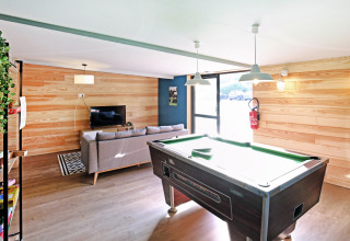 Sala comune con tavolo da biliardo, divano e TV presso Huttopia Baie du Mont St Michel in Bretagna, Francia.