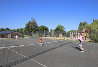 Børn spiller tennis på en udendørs bane ved Huttopia Baie du Mont St Michel feriepark i Bretagne, Frankrig.