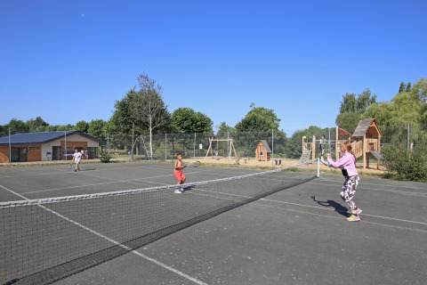 Børn spiller tennis på en udendørs bane ved Huttopia Baie du Mont St Michel feriepark i Bretagne, Frankrig.