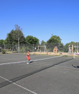 Kinder spielen Tennis auf einem Außenplatz im Huttopia Baie du Mont St Michel Ferienpark in der Bretagne, Frankreich.