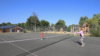 Niños juegan al tenis en una pista exterior del parque vacacional Huttopia Baie du Mont St Michel en Bretaña, Francia.