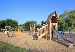 Spielplatz mit Holzrutsche, Schaukeln und Kletterstruktur im Ferienpark Huttopia Baie du Mont St Michel, Bretagne.