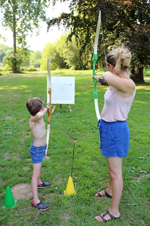 Volwassene en kind schieten met pijl en boog op grasveld in een vakantiepark in Bretagne, Frankrijk.
