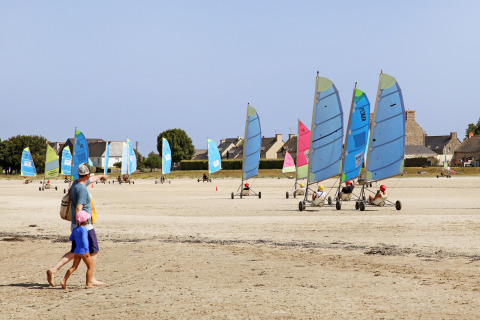 Un hombre y un niño caminan por la playa en Huttopia Baie du Mont St Michel, Bretaña, Francia, junto a carros a vela.