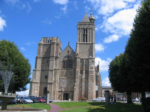 Kathedrale in Baguer Pican bei Dol de Bretagne, Bretagne, Frankreich, umgeben von Bäumen und Autos.