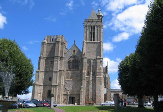 Cathedral in Baguer Pican near Dol de Bretagne, Brittany, France, surrounded by trees and parked cars.