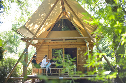 Gezin zit samen op het terras van een houten hut in Huttopia Rambouillet park, Île de France, Frankrijk.