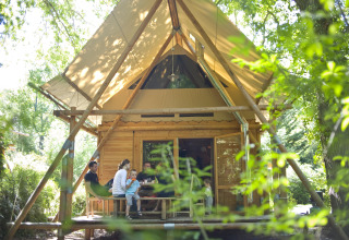 Familie sitzt gemeinsam vor einer Hütte im Grünen im Huttopia Rambouillet Ferienpark, Île de France.