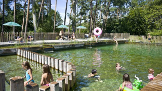 Kinder schwimmen und spielen in einem Naturpool im Ferienpark Huttopia Rambouillet, Île de France.