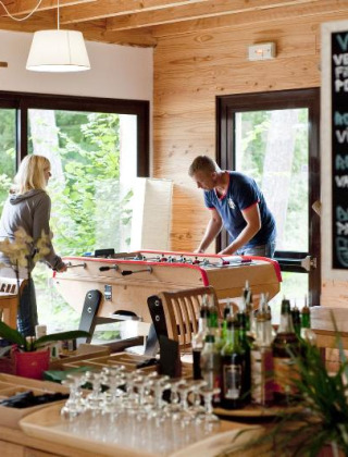 Vista interior en Huttopia Rambouillet donde unos huéspedes juegan futbolín en una acogedora cafetería.