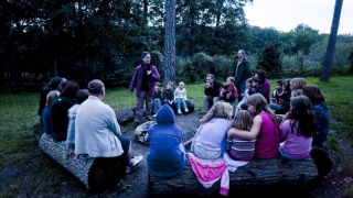 Kinder und Erwachsene sitzen am Lagerfeuer im Freien im Ferienpark Huttopia Rambouillet, Île de France.