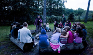Niños y adultos alrededor de una fogata en Huttopia Rambouillet, parque vacacional en Île de France, Francia.