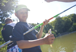 Niño pescando junto a un lago en un día soleado en Huttopia Rambouillet, Île de France, Francia.