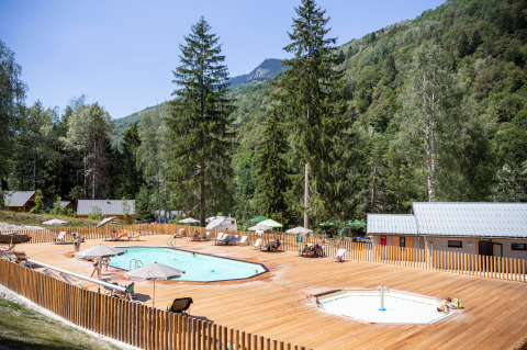Piscina al aire libre con tumbonas y sombrillas en Huttopia Bozel en Vanoise, rodeada de montañas verdes.