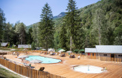 Piscine extérieure avec transats et parasols à Huttopia Bozel en Vanoise, entourée de montagnes verdoyantes.
