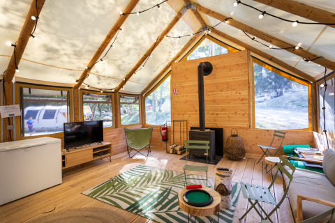Interior view of a cozy glamping tent with wooden floor, lounge area, string lights, and large windows.