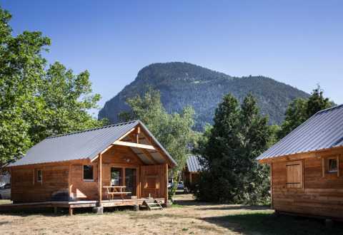 Cabañas de madera y mesa de picnic con montañas y árboles en Huttopia Bozel en Vanoise, Auvernia-Ródano-Alpes, Francia.