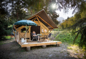 Familie entspannt auf Holzterrasse vor einem Kanadischen Safarizelt im Wald mit Sonne im Hintergrund.