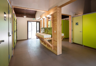 Modern, spacious restroom at Huttopia Bozel en Vanoise featuring green doors and wooden accents.