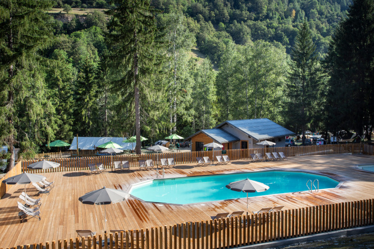 Piscine extérieure entourée de transats et parasols à Huttopia Bozel en Vanoise, Auvergne-Rhône-Alpes, France.