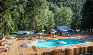 Piscina al aire libre con tumbonas y sombrillas en Huttopia Bozel en Vanoise, Auvergne-Rhône-Alpes, Francia.
