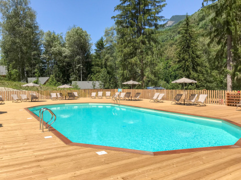 Piscina al aire libre con tumbonas y sombrillas sobre tarima de madera, rodeada de árboles en Auvergne-Rhône-Alpes.