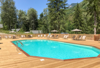 Outdoor swimming pool with sun loungers and umbrellas on a wooden deck, surrounded by trees in Auvergne-Rhône-Alpes.