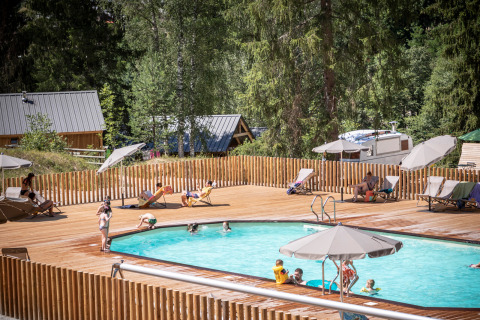 Børn og voksne slapper af ved poolen omgivet af skov på Huttopia Bozel en Vanoise feriepark i Frankrig.