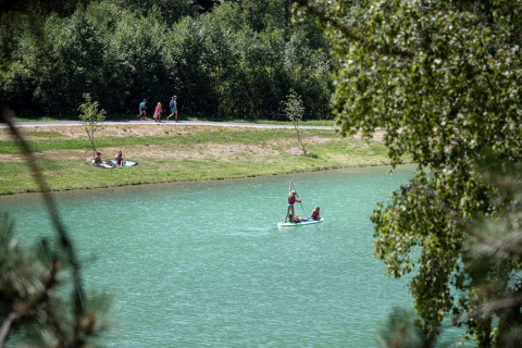Personas remando en lago cerca de Bozel, Francia, con árboles verdes y caminantes al fondo.