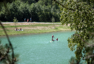 Menschen paddeln auf einem See bei Bozel, Frankreich, mit Bäumen und Spaziergängern am Ufer.