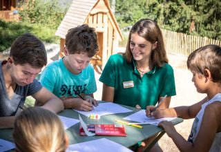 Børn og instruktør tegner sammen udendørs på Huttopia Bozel en Vanoise feriested i Frankrig.
