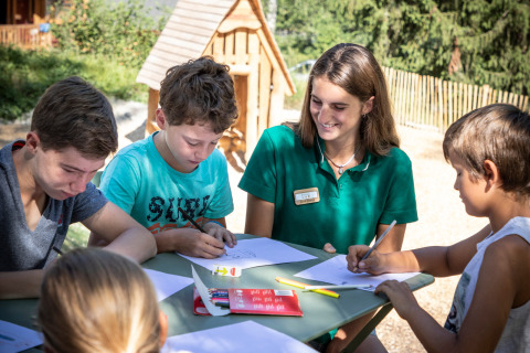 Kinder zeichnen draußen mit einer Betreuerin im Ferienpark Huttopia Bozel en Vanoise in Frankreich.