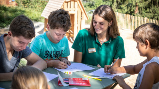 Niños dibujan junto a una monitora al aire libre en Huttopia Bozel en Vanoise, Francia.