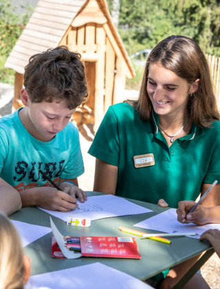 Niños dibujan junto a una monitora al aire libre en Huttopia Bozel en Vanoise, Francia.