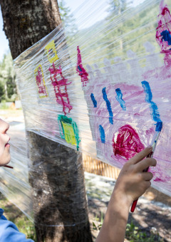 Niño pintando en film plástico entre árboles al aire libre en Huttopia Bozel en Vanoise, parque vacacional en Francia.