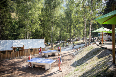 Visitantes juegan al ping-pong y se relajan entre árboles en Huttopia Bozel en Vanoise en Auvernia-Ródano-Alpes.