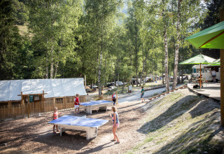 Feriegæster nyder bordtennis og aktiviteter blandt træerne på Huttopia Bozel en Vanoise i Auvergne-Rhône-Alpes.