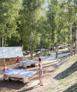 Visitantes juegan al ping-pong y se relajan entre árboles en Huttopia Bozel en Vanoise en Auvernia-Ródano-Alpes.