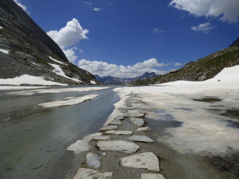 Stone path crossing melting snow and water in the mountains near Bozel, Auvergne-Rhône-Alpes, France.
