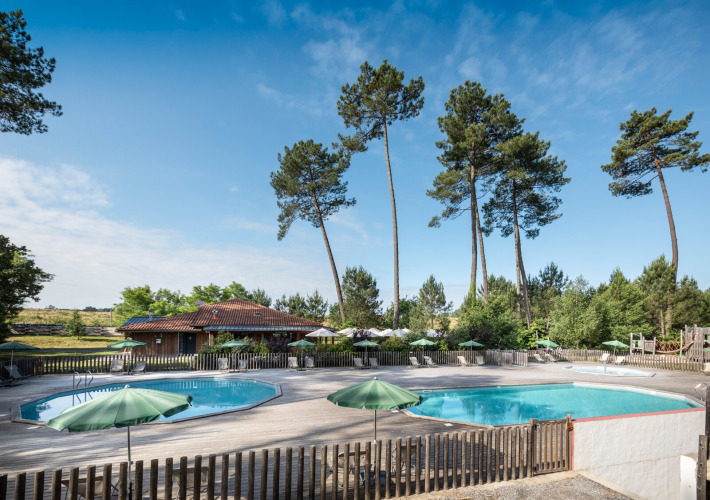 Outdoor swimming pools with green umbrellas, sun loungers, and tall pines at Huttopia Landes Sud, France.