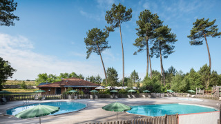 Piscinas exteriores rodeadas de pinos altos y sombrillas verdes en Huttopia Landes Sud, Nouvelle-Aquitaine.