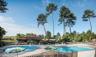 Foto von Außenpools mit grünen Sonnenschirmen und hohen Kiefern im Huttopia Landes Sud, Nouvelle-Aquitaine.