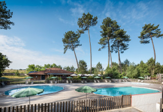 Outdoor swimming pools with green umbrellas, sun loungers, and tall pines at Huttopia Landes Sud, France.