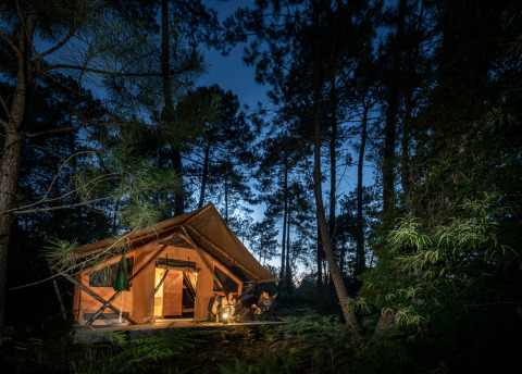 Tienda de glamping iluminada de noche en un bosque en Huttopia Landes Sud, Nouvelle-Aquitaine, Francia.
