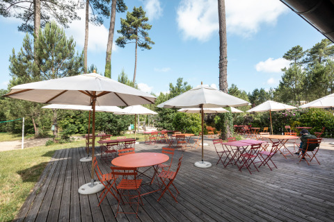 Terrasse extérieure avec tables rouges et parasols blancs au Huttopia Landes Sud, parc de vacances forestier.