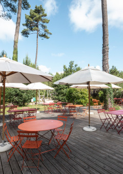 Zona de comedor al aire libre con mesas rojas y sombrillas blancas en Huttopia Landes Sud, Nueva Aquitania.