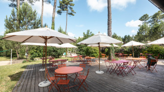 Zona de comedor al aire libre con mesas rojas y sombrillas blancas en Huttopia Landes Sud, Nueva Aquitania.